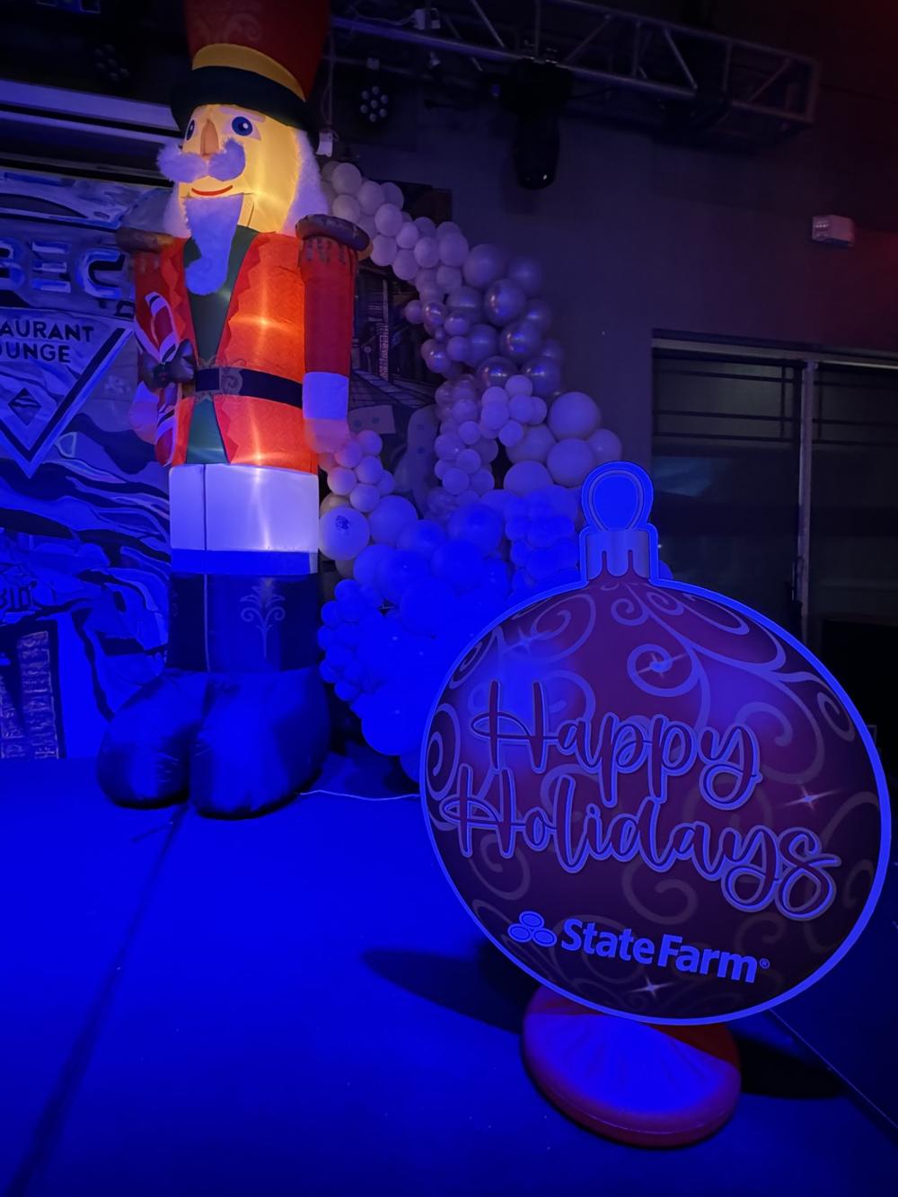 Giant nutcracker beside a white balloon garland and a State Farm Happy Holidays ornament sign